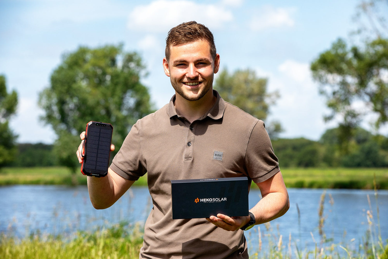 Man holding a solar powerbank and a box with 'Heko solar' branding outdoors.